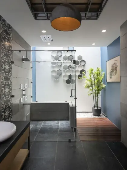 The master bathroom in Ashraya Residence is a spacious sanctuary in a refined palette of grey, black, and blue. The modern aesthetic blends functionality with style, featuring sleek finishes and a sculptural art piece.
