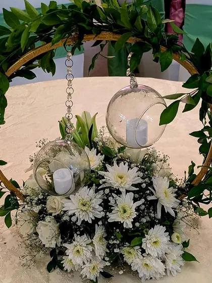 A modern and minimalist centerpiece, featuring a golden hoop with hanging glass orbs and candles, set within a bed of white chrysanthemums and baby's breath.