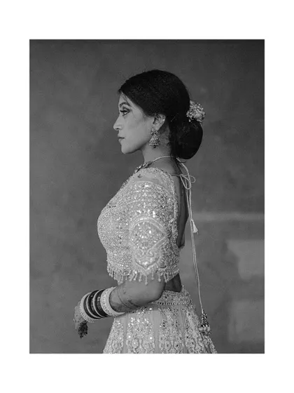 A classic black and white profile of a bride in her ornate lehenga. The focus on her silhouette and the texture of her dress creates a timeless and elegant portrait.