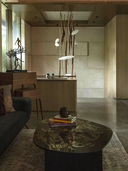 A view of the entrance lobby, where the sculptural Klove Grasshopper light descends towards a custom bar. The textured stone wall by Odyssey provides a rich backdrop, showcasing our focus on material and craftsmanship.