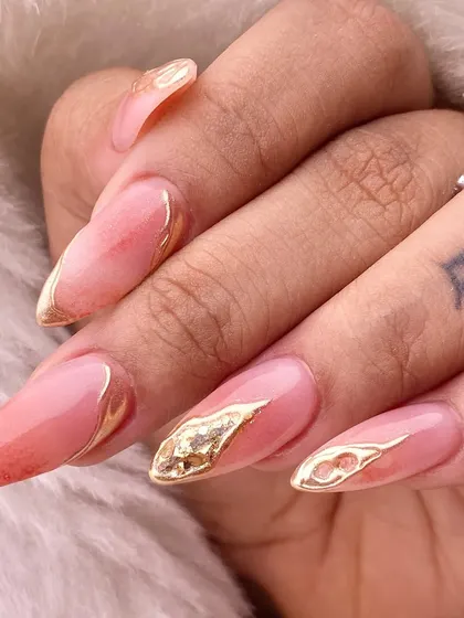 A touch of abstract luxury. This design features a peachy-pink base with accents of gold leaf and flowing gold lines, creating a warm and glamorous effect on almond-shaped nails.