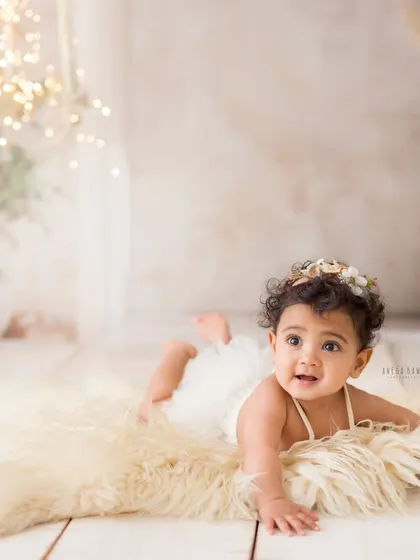 A sweet and curious expression during tummy time. This baby girl looks so lovely with her floral headband, lying on a soft fur rug in a beautifully lit studio.