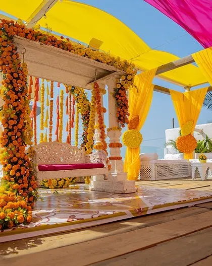 A classic Haldi setup, featuring a beautiful swing decorated with marigolds and a canopy of vibrant yellow and pink drapes. It's traditional, bright, and full of joy.