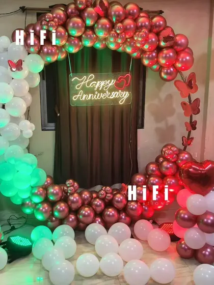A romantic first-anniversary decoration for a home. The setup includes a heart-shaped balloon arch in metallic red and white, a neon sign, and a light-up number '1'.