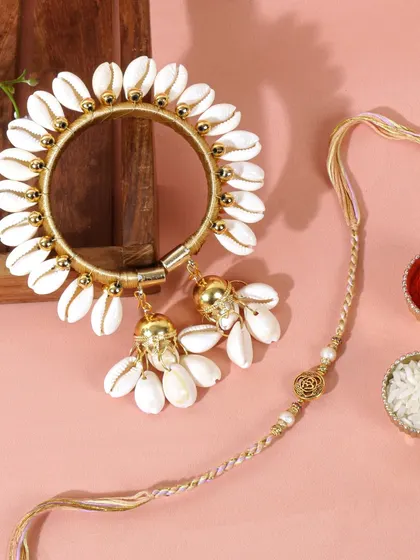 A clean and bright shot of the Lumba rakhi set against a soft pink background. This composition gives the traditional item a modern and fresh feel.