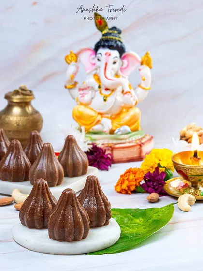 Chocolate modaks styled with a Ganesha idol for the festival. The clean, white marble background gives a modern and pure feel to this traditional sweet.