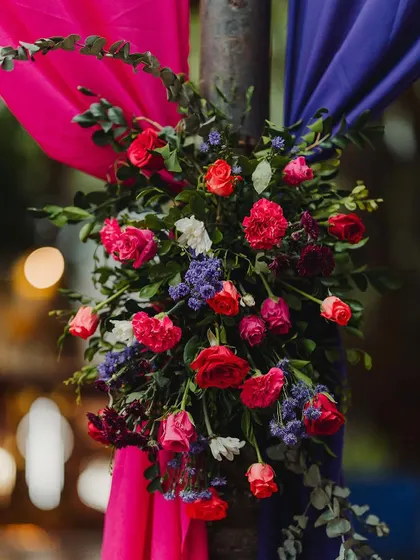 A lush floral arrangement of red and purple flowers is tied to a pillar draped in colorful fabric, adding to the rich, layered look of the Moroccan theme.