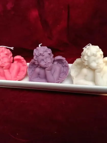 A set of three cherub or angel-shaped candles in pink, purple, and white.