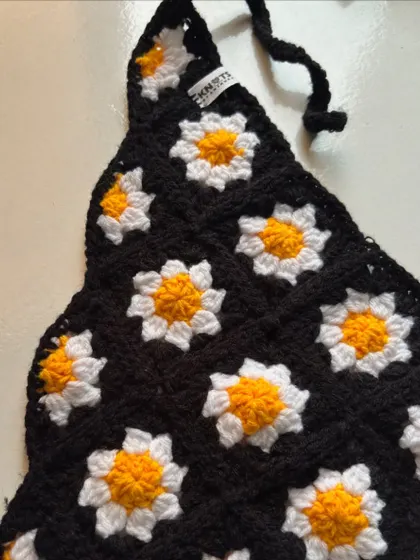 A closer look at the daisy granny square pattern on the black crochet bandana. Each little flower is stitched with care.