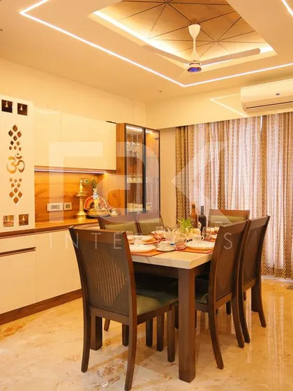 A modern dining area featuring a custom pooja unit with "Om" carvings. The design seamlessly blends spiritual elements with contemporary furniture and lighting.