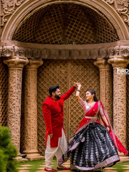 A playful dance in front of a grand, ornate doorway. The couple's red and black traditional outfits create a striking and dramatic visual.