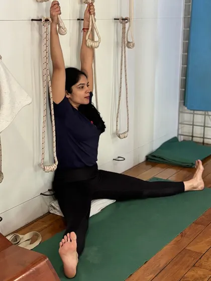 This student is using the wall ropes to deepen her stretch in Upavistha Konasana. The ropes provide traction, helping to open the hips and lengthen the inner thighs and spine safely.
