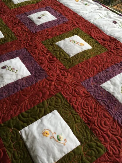 A beautiful quilt with embroidered floral blocks, set in a rich, warm-toned patchwork.