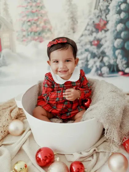 A perfect Christmas smile! This little girl looks absolutely adorable in her plaid dress, sitting in a bucket surrounded by festive ornaments.