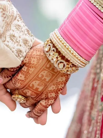 A close-up of the couple's hands, showing the bride's mehendi and bangles.