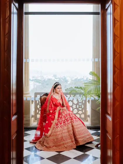 A classic bridal portrait, with the bride seated in a doorway, the light catching her red lehenga perfectly.