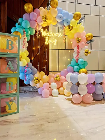 A rainbow-themed "Welcome Baby" decoration with a pastel balloon ring, neon sign, and 'BABY' blocks.