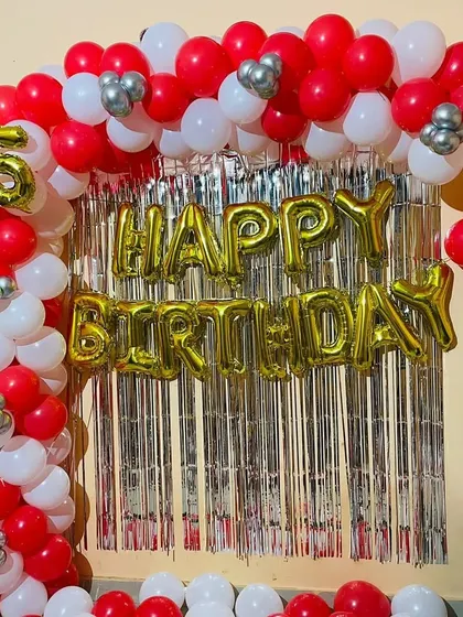 A classic 25th birthday backdrop with a red, white, and silver balloon arch over a foil curtain.