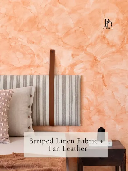 Texture is key to creating a warm, inviting bedroom. Here, a custom headboard made of striped linen fabric with a tan leather strap is set against a beautiful terracotta-toned textured paint wall.