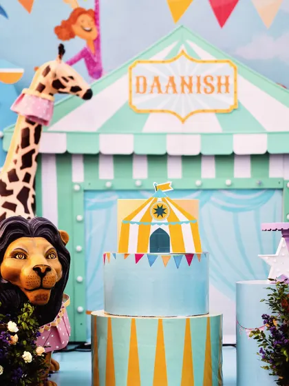 The beautiful, multi-tiered carnival cake is the star of the dessert table. Its design perfectly matches the pastel blue and yellow circus theme.
