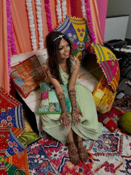 The happy bride Mayuri, surrounded by colorful decor, proudly displaying her intricate bridal mehendi.