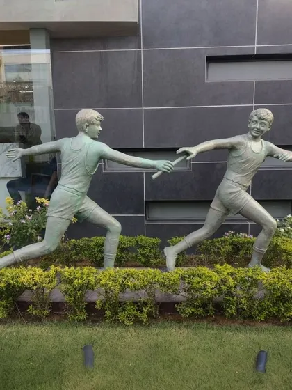 A side profile of the relay race sculpture, emphasizing the motion and energy of the two figures.