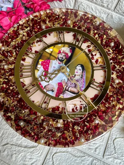 A full view of the varmala preservation clock, showing the rich bed of red rose petals and gold flakes. The couple's photo and wedding date are sealed in the center.