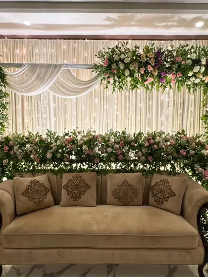 An elegant stage for a Nikkah ceremony, featuring a floral arch and a backdrop of fairy lights.
