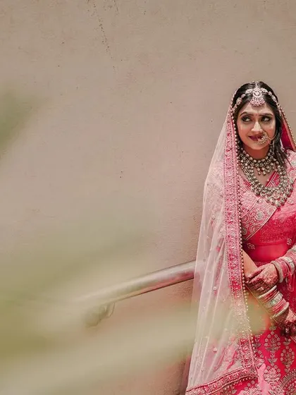 A creative bridal portrait taken from a low angle with foliage in the foreground. The bride's expression is calm and beautiful as she stands on a staircase.