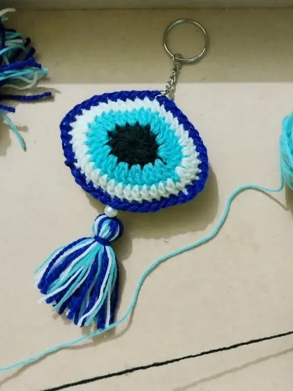 The making of an evil eye keychain. You can see the yarn and the finished product coming together, all crafted by hand.
