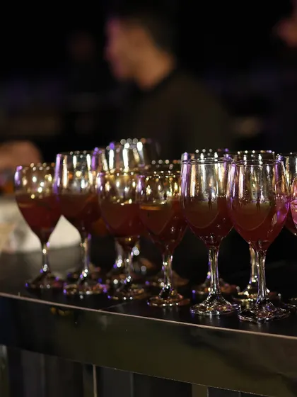 Glasses of a rich, red mocktail are lined up on the bar, ready to be served. The warm lighting reflects beautifully in the glassware, creating an inviting and celebratory atmosphere.