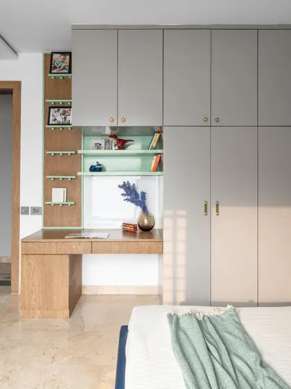 The integrated study nook and wardrobe unit in the kid's room. This custom piece maximizes space by combining a desk, open shelving, and full-height closets, all while maintaining the room's fun and modern aesthetic.