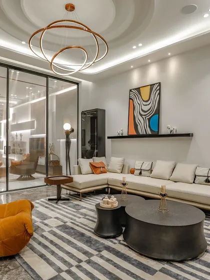 This living space in Vikaspuri features a bold geometric rug, a comfortable sectional sofa, and a striking orange lounge chair. I use pops of color and sculptural furniture to add personality to a room.