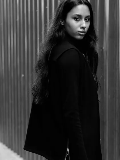 An urban portrait in black and white. The corrugated metal wall provides a gritty, textured background that contrasts with the model's soft expression.