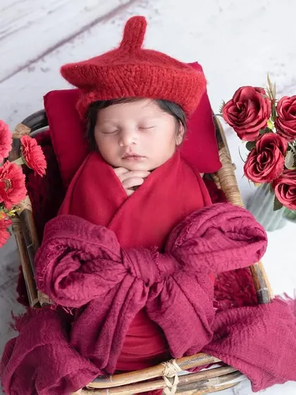 A pop of red! This newborn looks striking in a red wrap and hat, nestled in a basket.