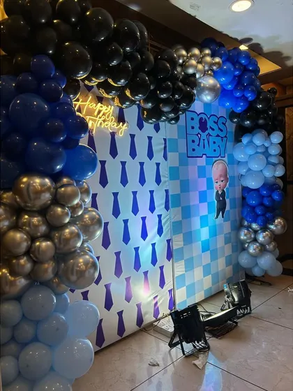 A close-up of a Boss Baby themed party backdrop. The design includes a custom printed wall and a balloon arch in shades of blue, black, and silver, perfect for photos.