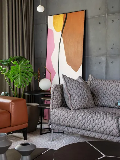 A close-up of the living room's material palette, showing the contrast between the soft, textured sofa, the smooth leather, and the raw concrete wall.
