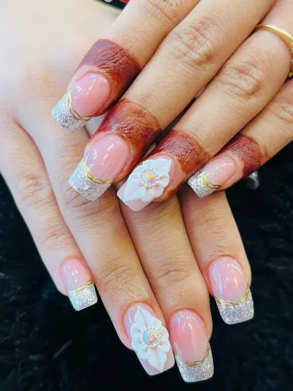 Perfect for a bride, these square-tipped extensions feature a delicate silver glitter French design. The look is made even more special with a stunning 3D white floral accent nail, complete with a crystal center.