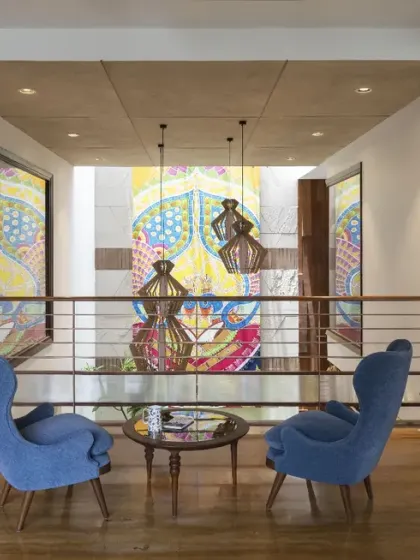The first-floor lounge in Ashraya Residence overlooks the central courtyard. The double-height space, with its dramatic painting and custom chandeliers, creates a strong visual connection with the floor below.
