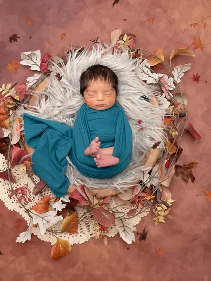 A beautiful autumn-themed portrait with a baby wrapped in a deep teal swaddle, contrasting beautifully with the warm tones of the fall leaves.