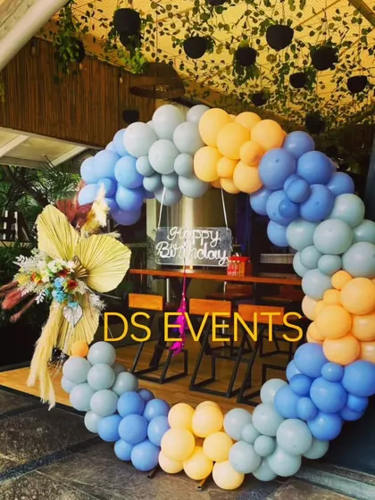 A unique circular balloon wreath in shades of blue and yellow, perfect for an outdoor or rustic-themed party. The arrangement is accented with dried floral elements, creating a beautiful and modern photo backdrop.