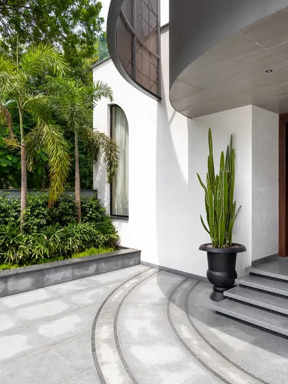 The curved entrance of the Juneja Residence, framed by lush palm trees and minimalist landscaping. We use organic forms and natural elements to soften modern architecture and create a harmonious entry sequence.