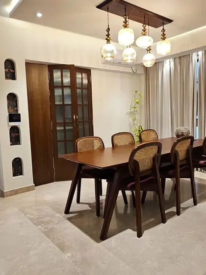 A beautiful dining room from our project at 77-degree Divyashree. The space features a large wooden table, cane chairs, and statement lighting.