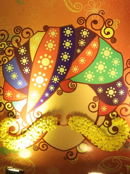 A colorful, lighted installation of a man's face with a turban and a mustache made of marigolds, part of a quirky decor theme.
