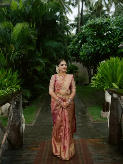 A full-length portrait of the South Indian bride, walking on a path surrounded by lush greenery. Her grace and beautiful attire are the focus.
