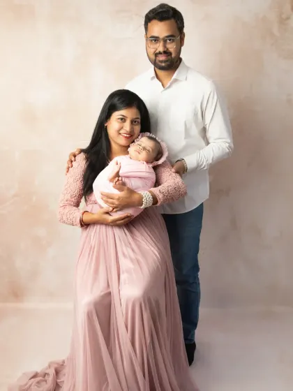 A full-length portrait of a new family of three, standing together in the studio while the mother holds their precious newborn.