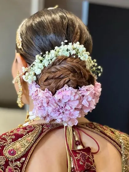 A back view of a braided bun adorned with a combination of baby's breath and pink hydrangeas. The texture and colors create a beautiful and romantic bridal updo.