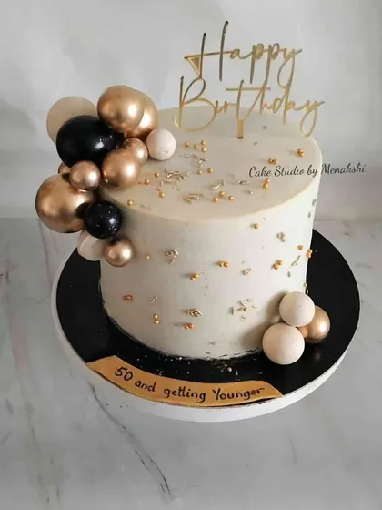 Celebrating "50 and getting younger" with this stylish no-fondant cake. The black, white, and gold spheres, along with gold leaf flakes, create a chic and celebratory design.