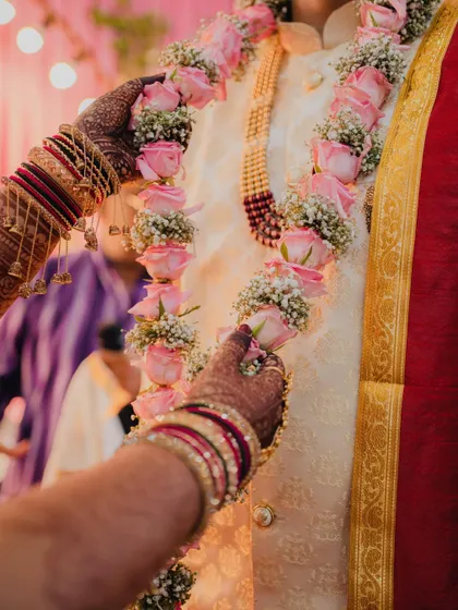 A close-up of the Varmala ceremony, focusing on the bride's hands placing the rose garland on the groom.
