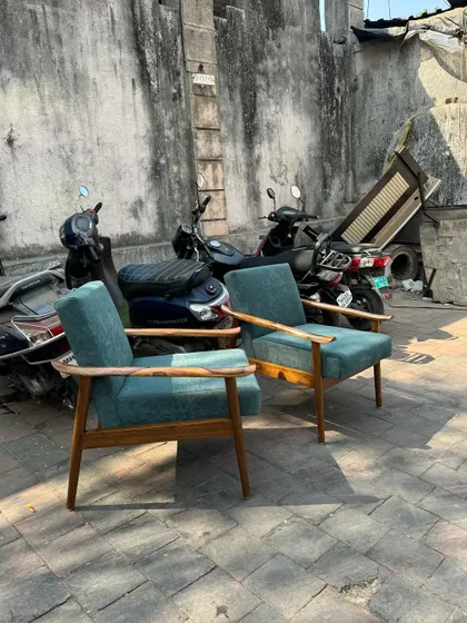 A pair of classic mid-century style lounge chairs with solid teak frames and teal upholstery.